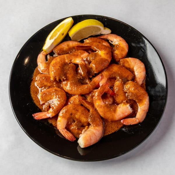 A black plate filled with shrimp coated in a rich, reddish-brown sauce, garnished with lemon wedges.
