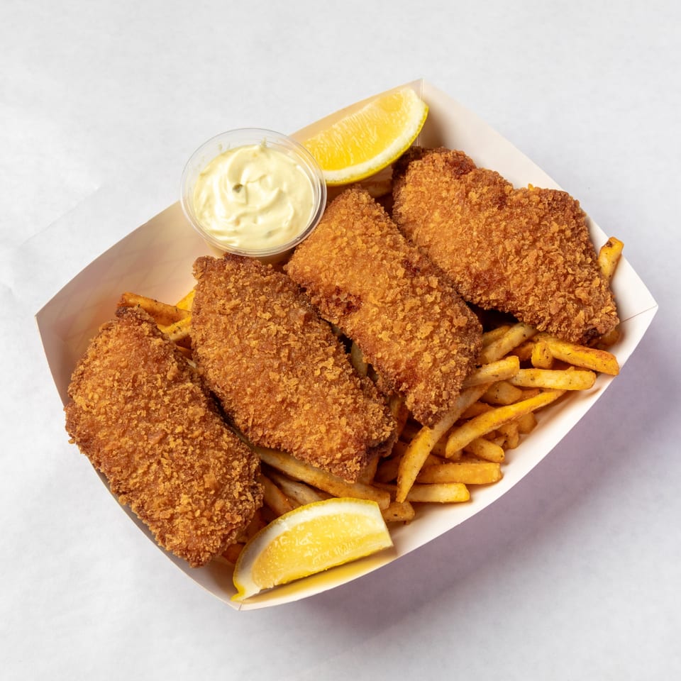 Crispy fried fish and chips in a paper tray, with tartar sauce and lemon wedges.
