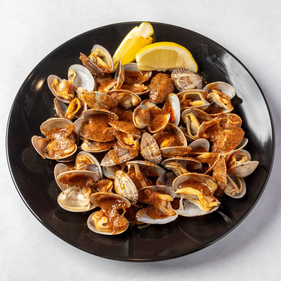 A black plate filled with steamed clams in a rich brown sauce, garnished with two lemon wedges.