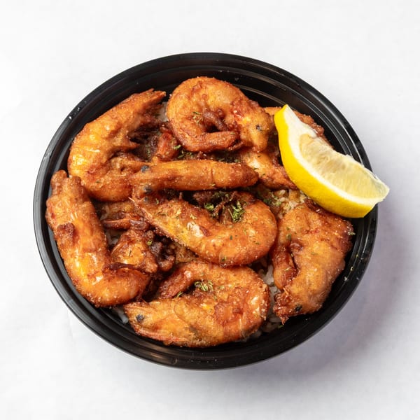 Crispy fried shrimp with herbs and a lemon wedge in a black bowl on a white surface.