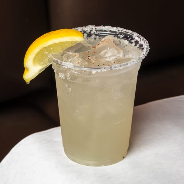 A lemon margarita in a plastic cup with a salted rim and chili powder, garnished with a lemon slice.