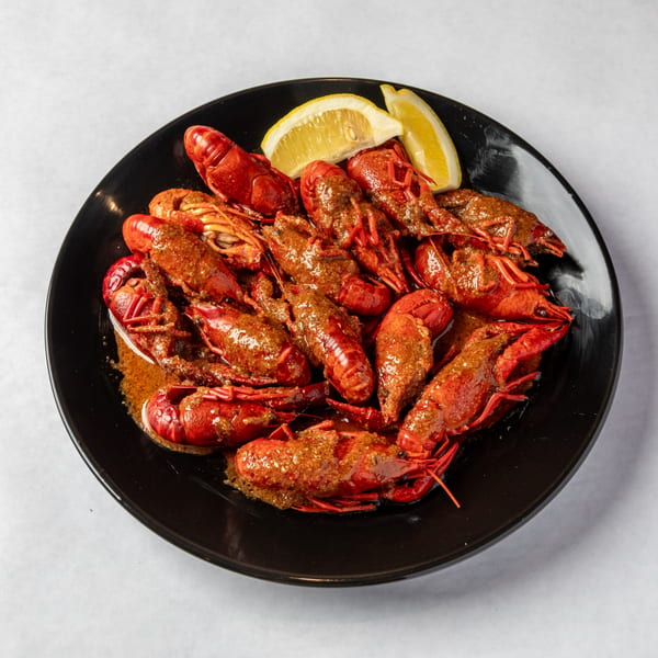 A black plate filled with red crawfish covered in a rich, savory sauce, garnished with lemon wedges.