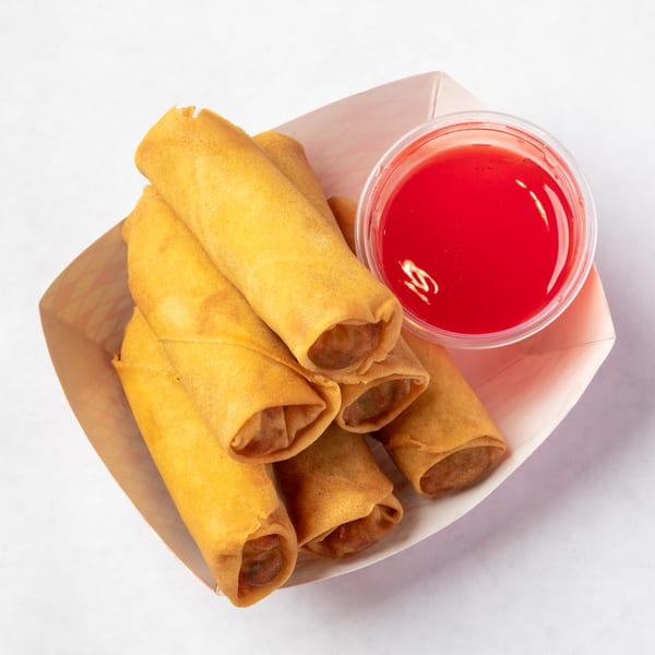 Golden-brown egg rolls in a paper tray with a side of bright red sweet and sour sauce.